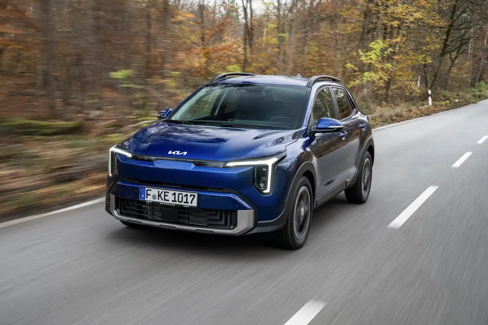 Blauwe Kia Niro op bosweg in de herfst, modern en dynamisch ontwerp.