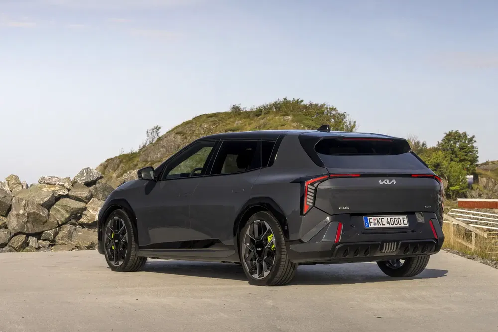 Kia EV9 SUV noir, arrière profil, stationné devant des rochers dans un cadre côtier.