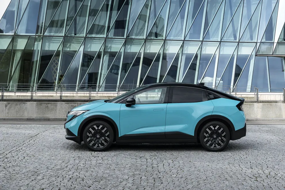 Nissan Ariya 2023 blauw voor een modern glazen gebouw.