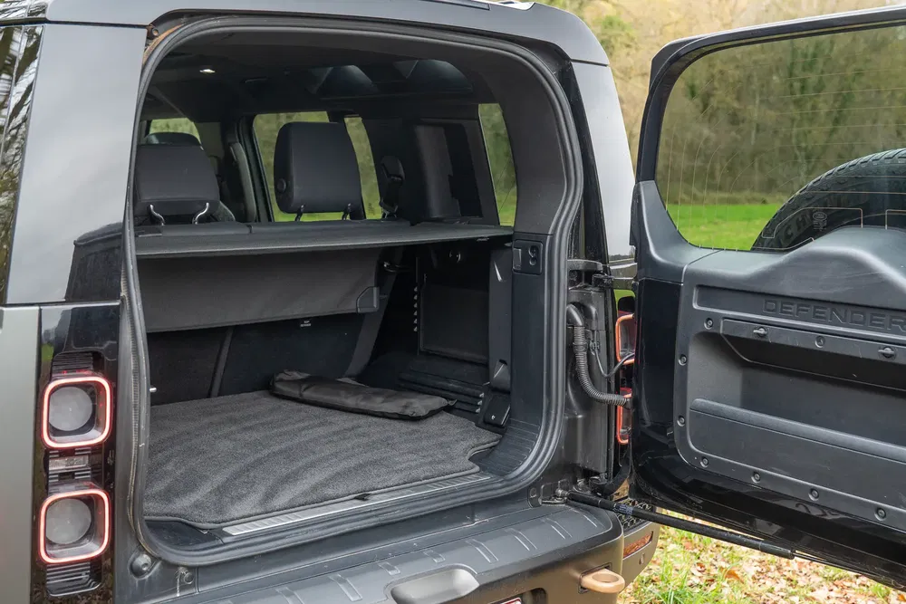 Coffre spacieux du Land Rover Defender avec porte arrière ouverte et siège rabattable.