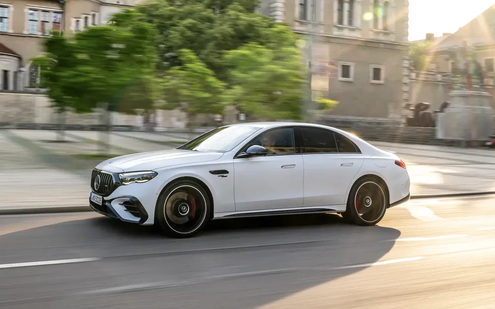 Mercedes AMG berline blanche, roulant en ville au coucher du soleil.