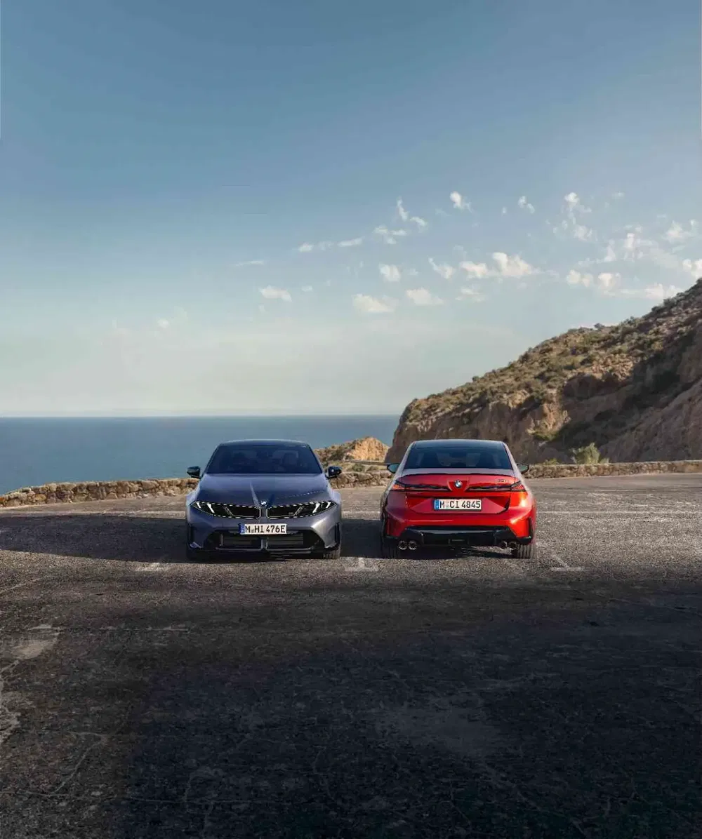 Deux BMW stationnées sur une route côtière, avec vue sur la mer et falaise.