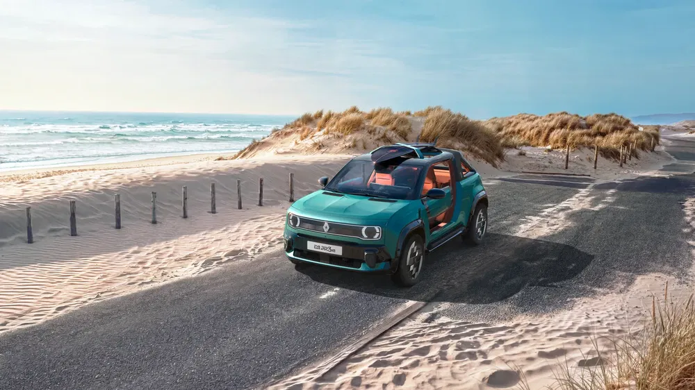 Renault strandbuggy op zonnige kustweg met duinen en oceaan op de achtergrond.