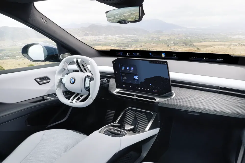 Moderne BMW-interieur met opvallend stuur en centraal touchscreen met panoramisch uitzicht.