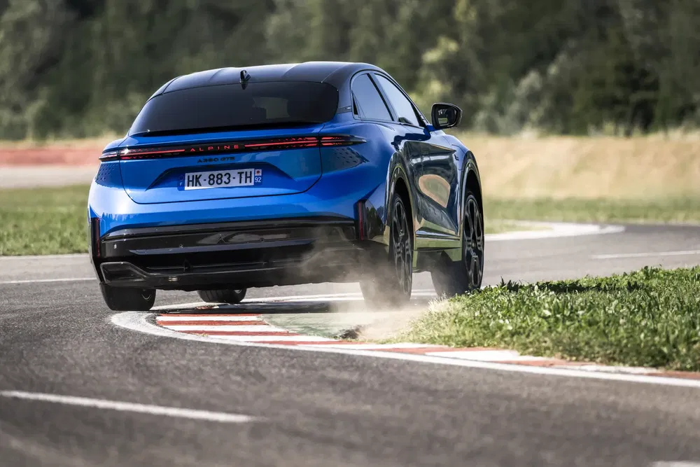 Voiture Alpine bleue prenant un virage sur piste avec poussière volant.