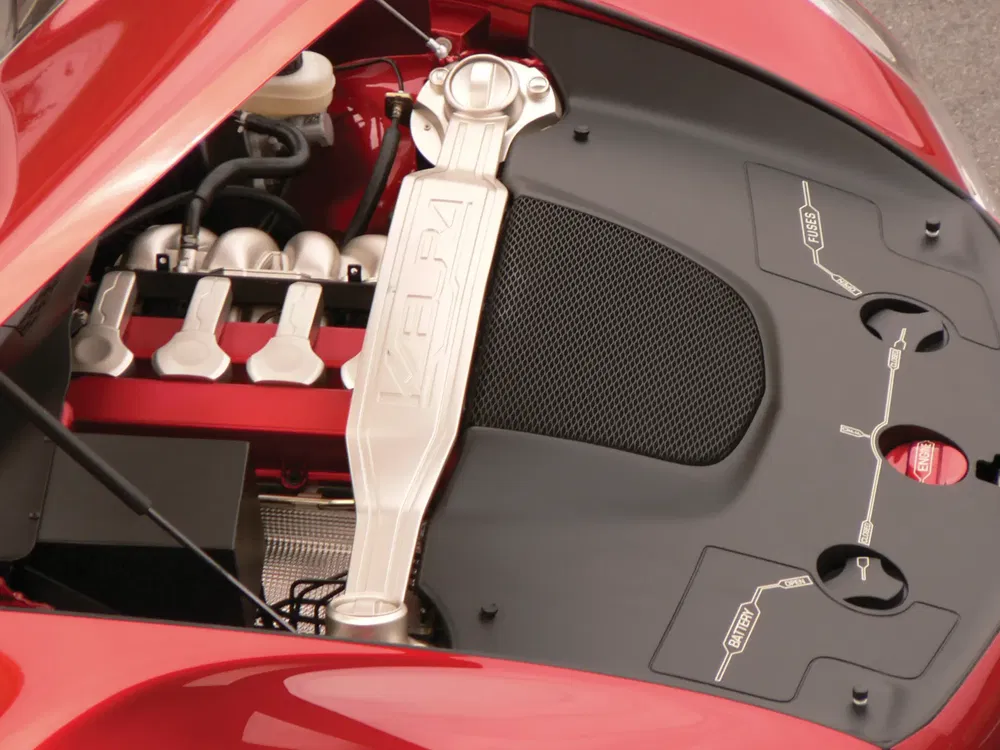 Moteur V12 Ferrari sous un capot rouge, composants mécaniques visibles.