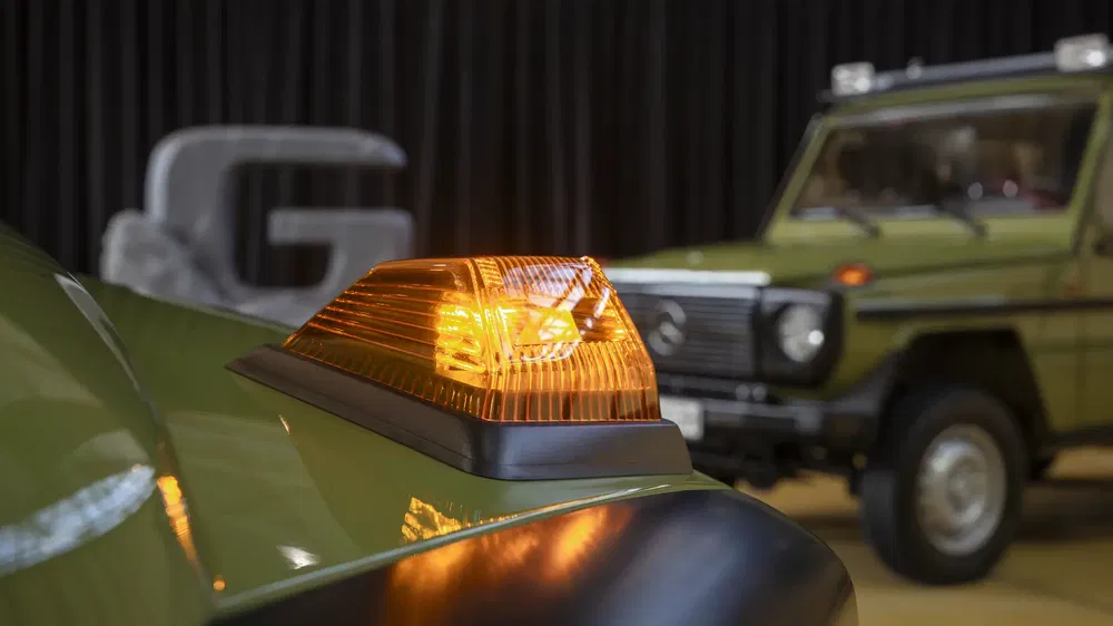 Groene Mercedes-Benz G-Klasse met knipperlicht aan, onscherpe achtergrond, moderne omgeving.