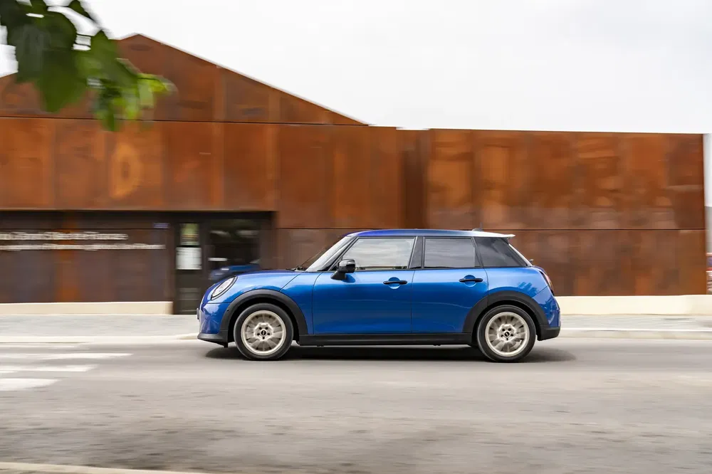 Mini Cooper bleu roulant devant un bâtiment moderne en acier Corten.