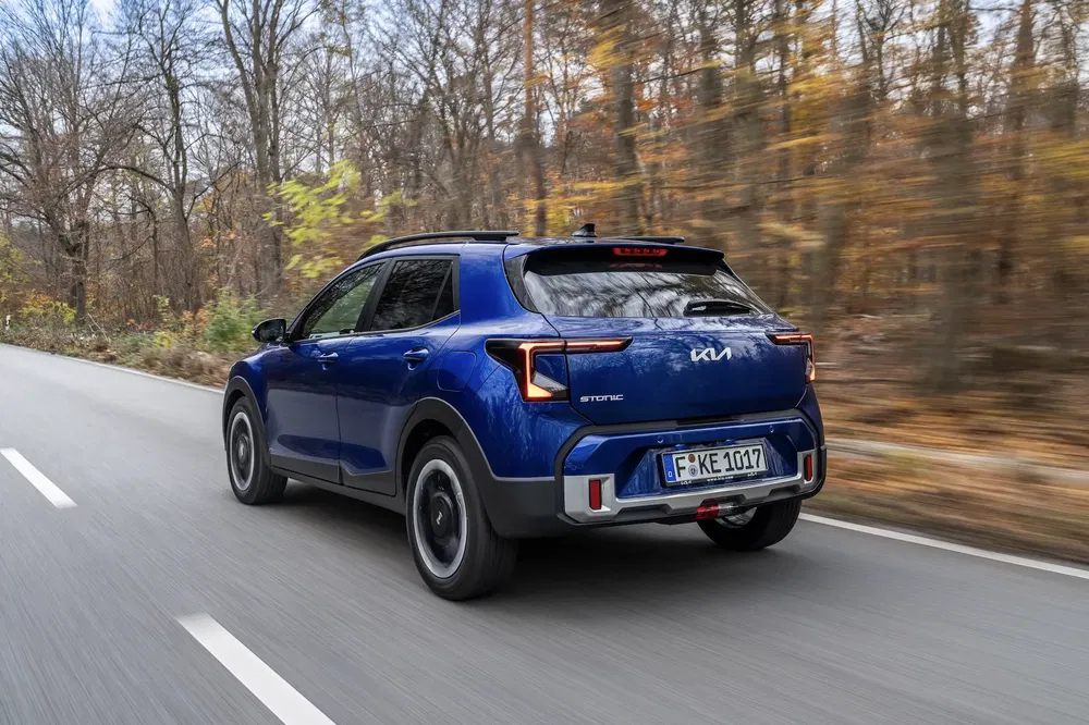 Kia Stonic blauw rijdt op weg door herfstbos.