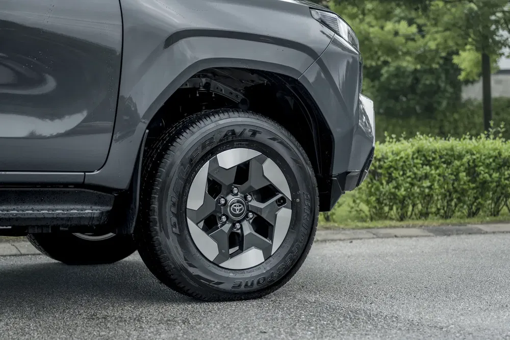 Pneumatique Toyota sur SUV gris, stationné sur route mouillée, avec feuillage en arrière-plan.