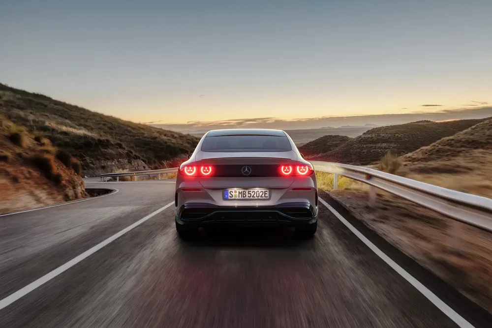Mercedes-Benz sur route sinueuse au crépuscule avec feux arrière allumés.