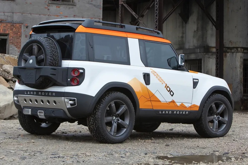 {"fr":"Land Rover Defender concept blanc et orange, design extérieur moderne en fond industriel.","nl":"Witte en oranje Land Rover Defender concept met modern design in industriële omgeving."}