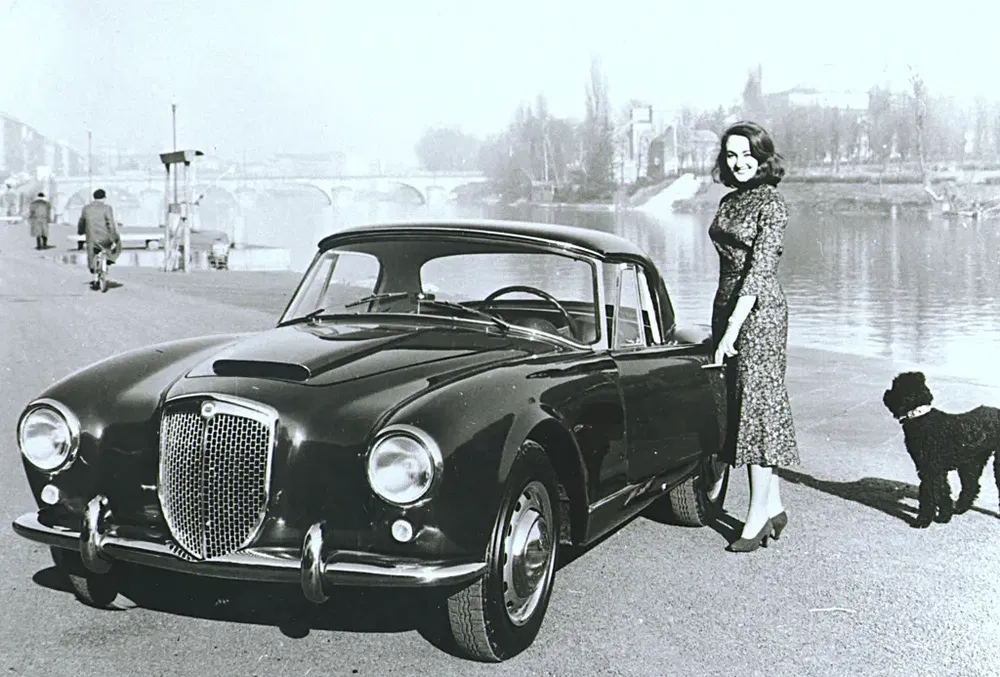Classique Lancia Aurelia B20 avec femme élégante et chien en bordure de rivière.