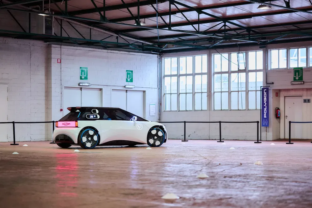 Voiture autonome blanche dans un entrepôt avec éclairage industriel et cônes de signalisation.