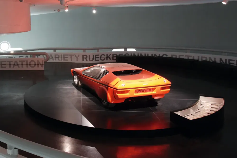 Concept car BMW Turbo orange exposé dans un musée moderne, éclairage tamisé spectaculaire.