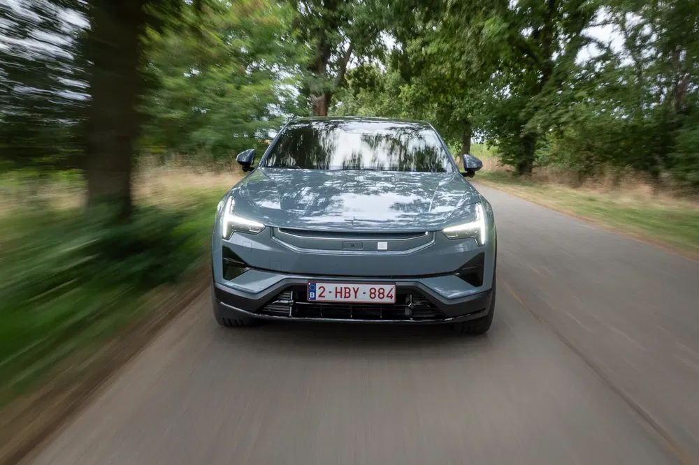 Moderne elektrische auto rijdt op een boomrijke weg op een zonnige dag.
