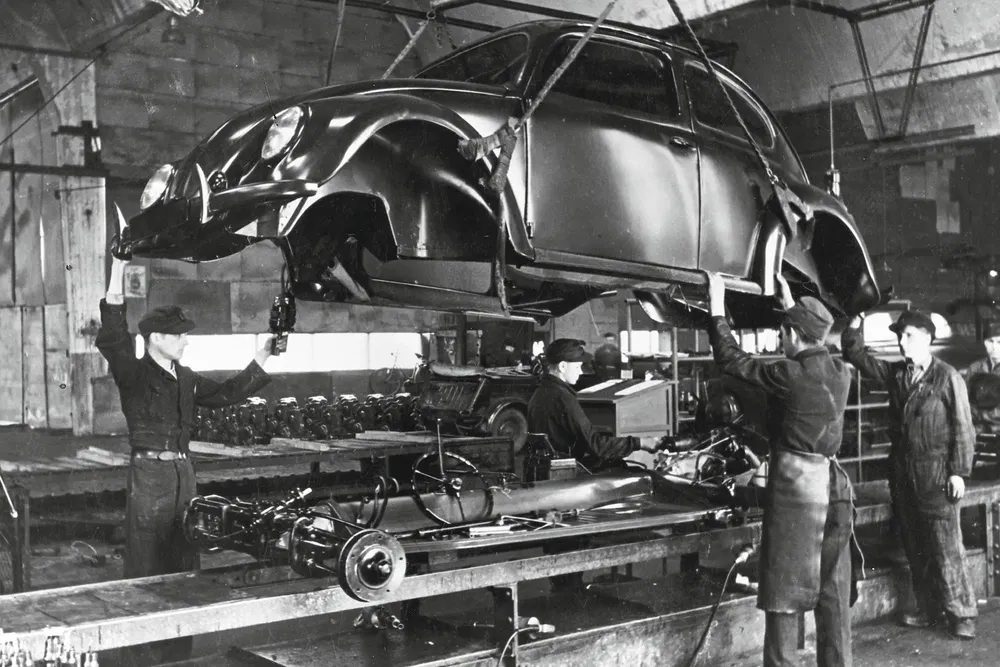 Usine assemblant une Volkswagen Beetle vintage avec des ouvriers sur une chaîne de montage.