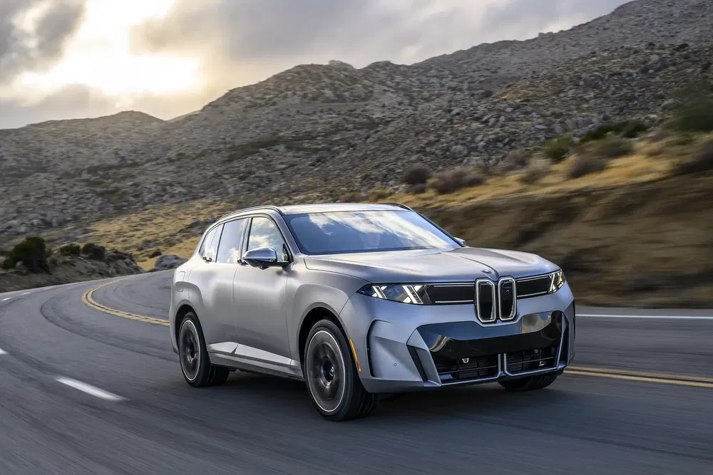 Zilveren BMW X5 rijdt op een bochtige bergweg onder een bewolkte lucht.