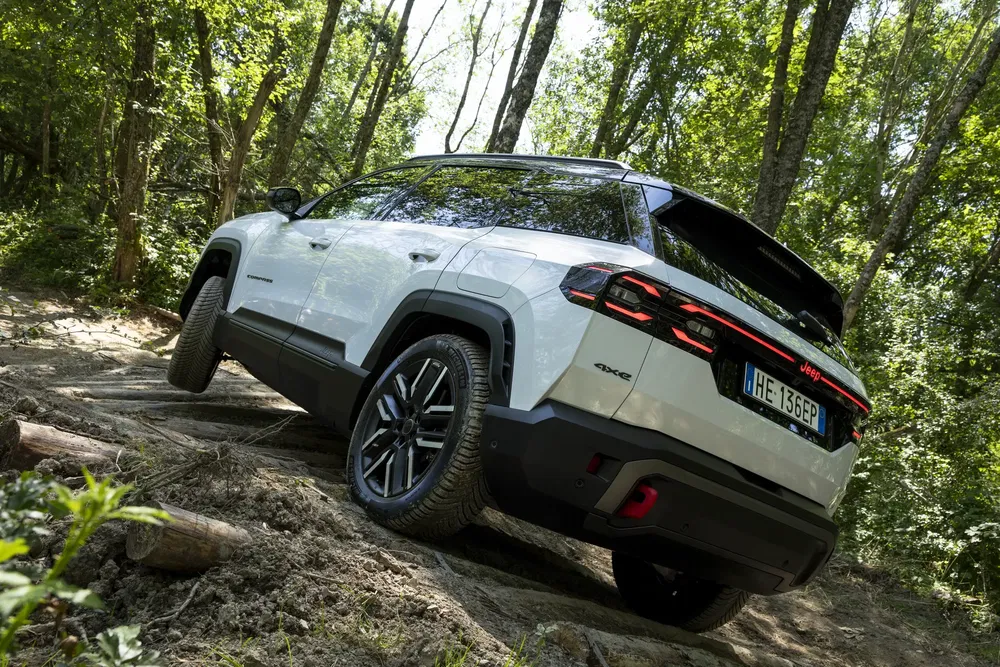Jeep Grand Cherokee blanc sur terrain accidenté en forêt, showcasing ses capacités tout-terrain.