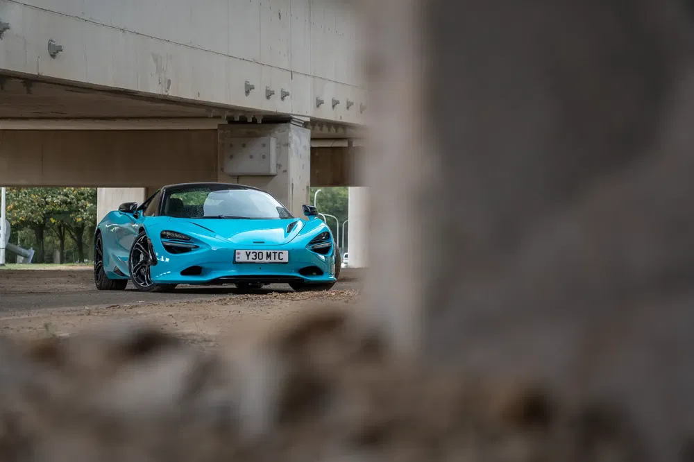 {"fr":"Voiture McLaren bleue garée sous un pont, vue à travers un cadre de béton.","nl":"Blauwe McLaren auto geparkeerd onder een brug, gezien door een betonnen kader."}