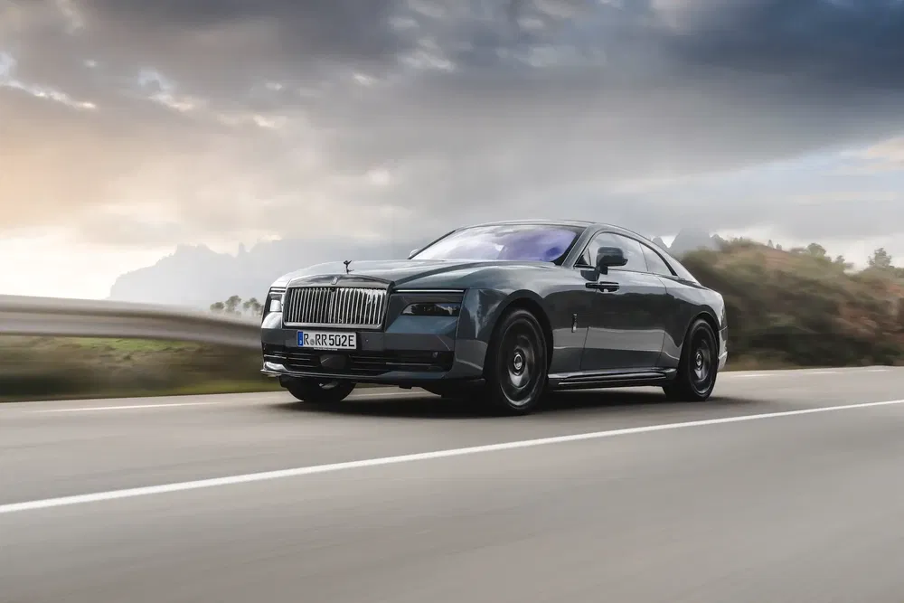 Rolls-Royce Spectre roulant sur une route, sous un ciel nuageux matin.