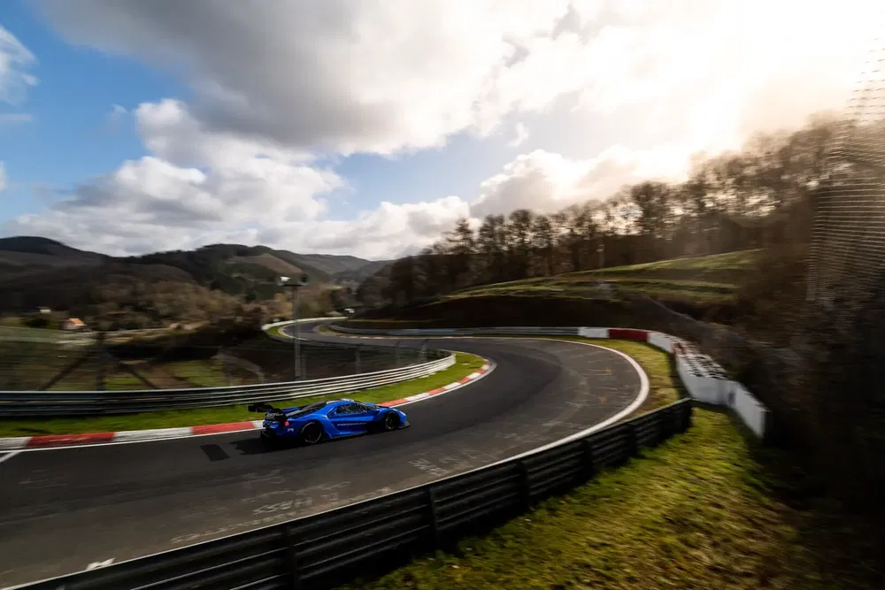 Voiture de sport bleue sur circuit sinueux entouré de verdure et montagnes.