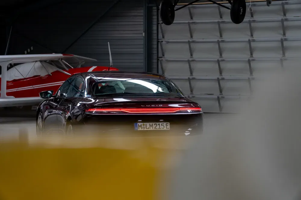 Voiture Lucid Air dans un hangar, avion rouge et blanc en arrière-plan.