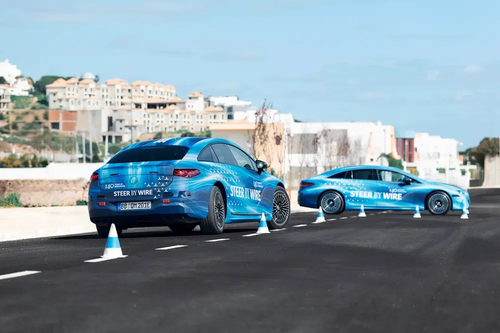 Twee blauwe Mercedes-Benz EQS tijdens testrit met verkeerskegels langs de weg.