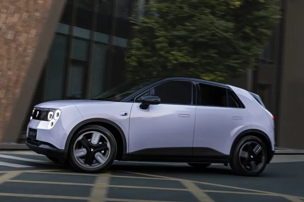 Voiture électrique blanche, design moderne, jantes noires, devant un immeuble en ville.