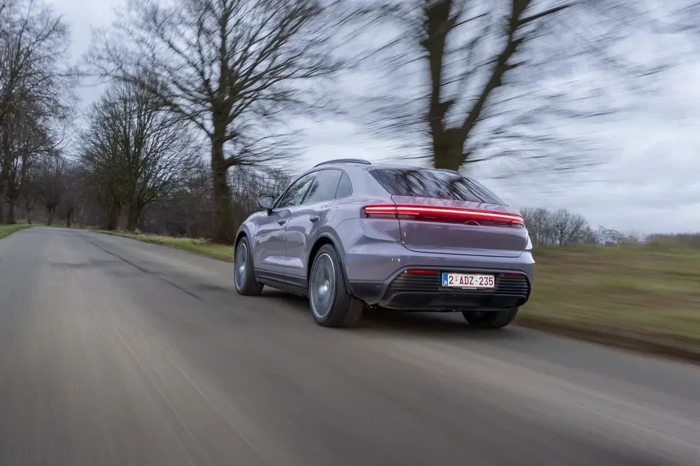 Porsche Cayenne 2024 roulant sur une route bordée d'arbres, ciel nuageux en arrière-plan.