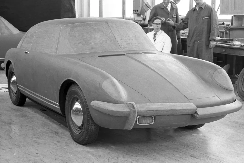 Prototype en argile de Porsche 911 dans un atelier, ingénieurs en arrière-plan.