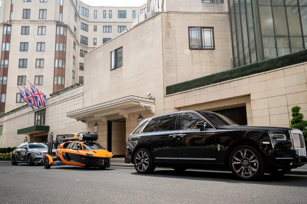 Rolls-Royce Cullinan noire et voiture volante PAL-V orange devant un hôtel londonien.