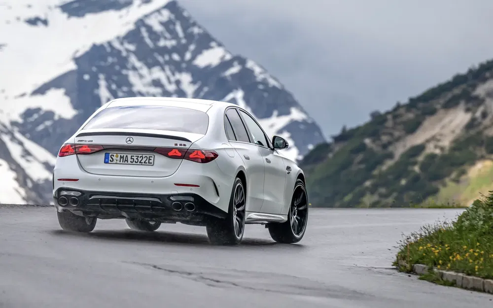 Mercedes-AMG E53 blanche sur route sinueuse de montagne enneigée, arrière dynamique en mouvement.