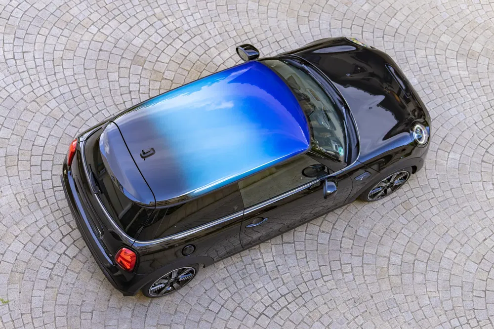 MINI Cooper noire au toit dégradé bleu, sur pavé circulaire.