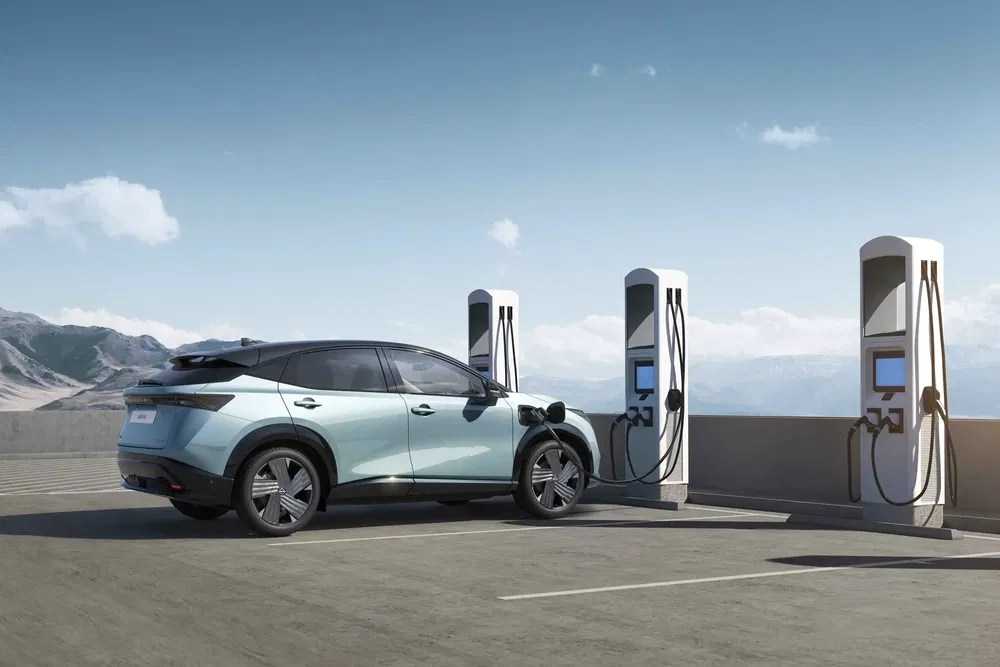 SUV électrique en recharge avec bornes, ciel dégagé et montagne en arrière-plan.