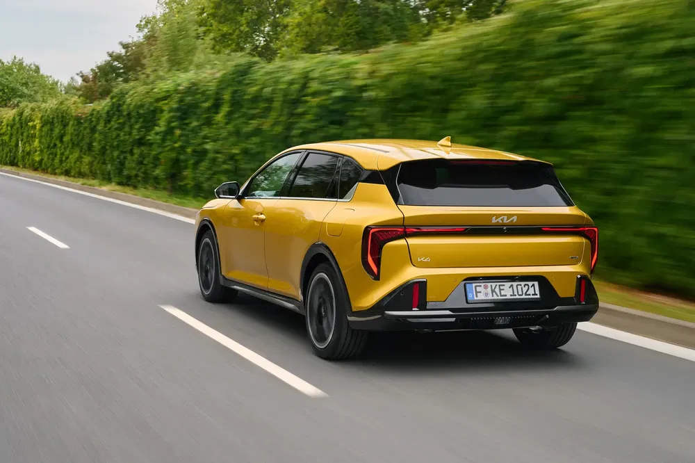 Kia jaune circulant sur route bordée d'arbres, vue arrière de l'élégant design moderne.