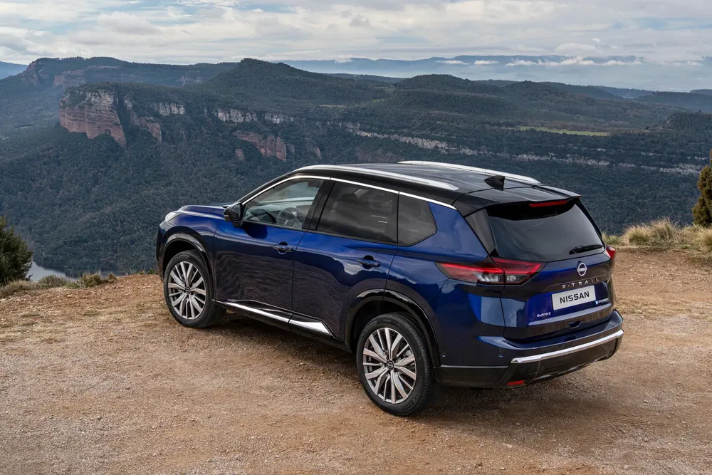 Blauwe Nissan X-Trail met uitzicht op adembenemend berglandschap.