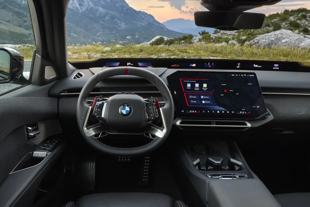 Intérieur de BMW moderne avec tableau de bord numérique, volant élégant, paysage montagneux en arrière-plan.