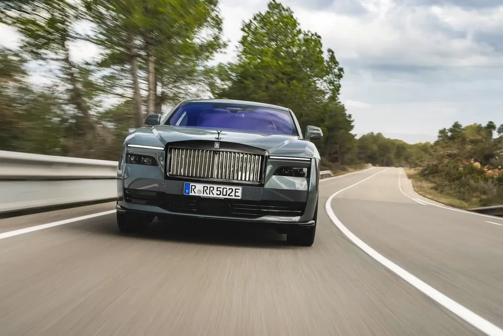Rolls-Royce électrique en mouvement rapide sur une route sinueuse entourée d'arbres.