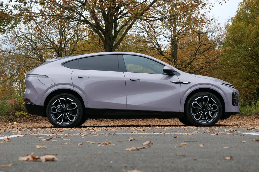Profil latéral d'un SUV moderne sur une route automnale, ciel gris et arbres dénudés.