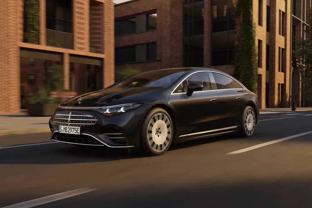 Mercedes-Benz EQS noir roulant dans une rue entourée de bâtiments modernes en brique.