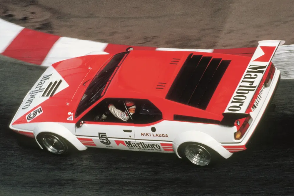 BMW M1 rouge sur circuit avec livrée Marlboro et nom Niki Lauda.