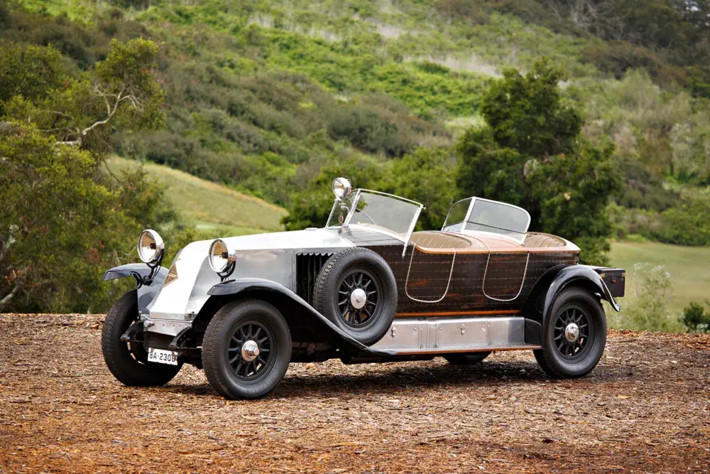 Voiture vintage Hispano-Suiza sur sol boisé avec arrière-plan de forêt verdoyante.
