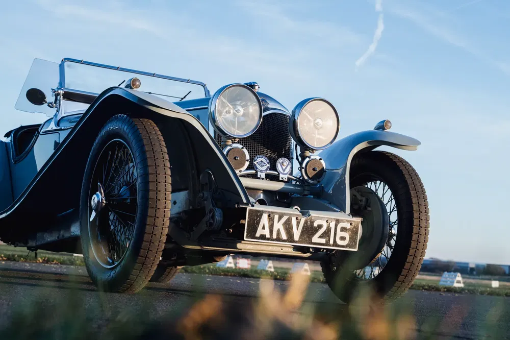 Jaguar SS100 classique avec phares ronds et plaque AKV 216, ciel dégagé en arrière-plan.