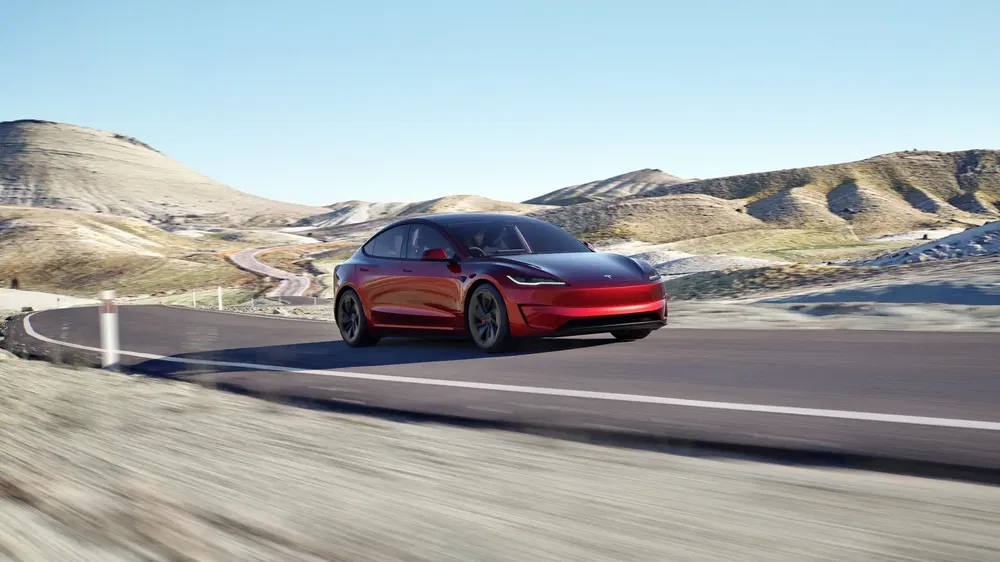 Tesla rouge brillant sur route de montagne sinueuse par temps ensoleillé.