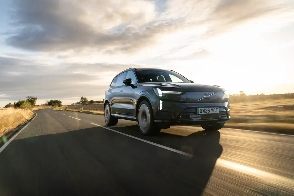 SUV électrique Volvo EX90 sur route de campagne au coucher du soleil, performance dynamique.
