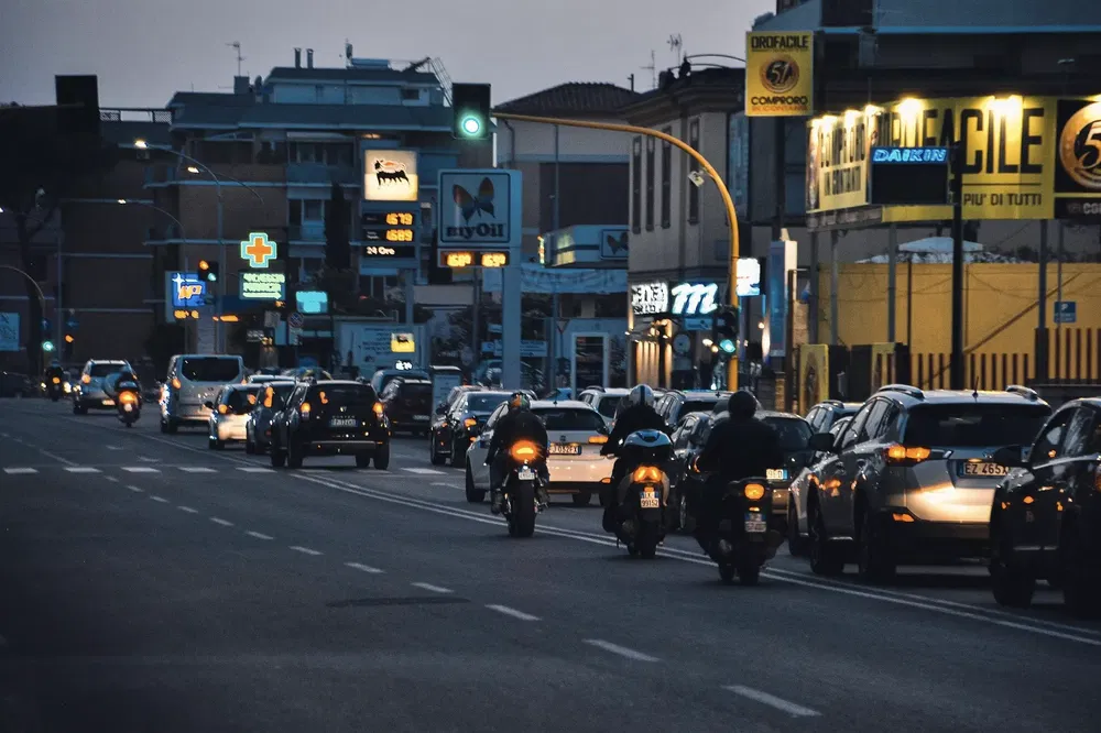 Voitures et motos sur une route urbaine éclairée au crépuscule avec panneaux lumineux.