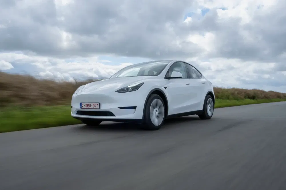 Tesla Model Y blanche roulant sur une route de campagne sous un ciel nuageux.