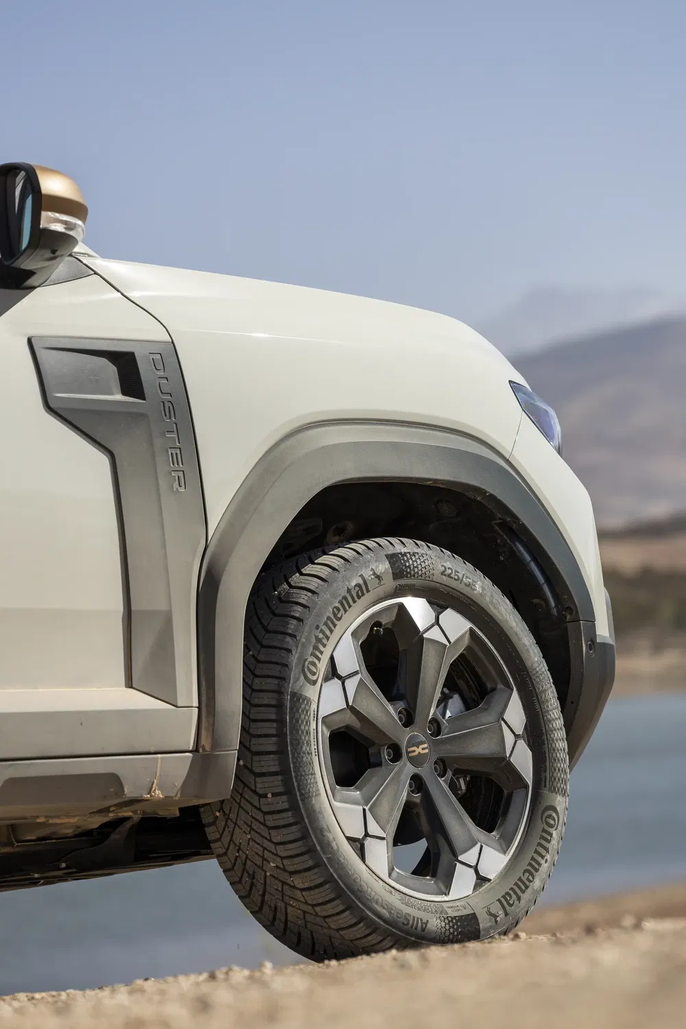 Zijaanzicht van witte Dacia Duster met Continental-band, natuurlijke woestijnachtergrond.