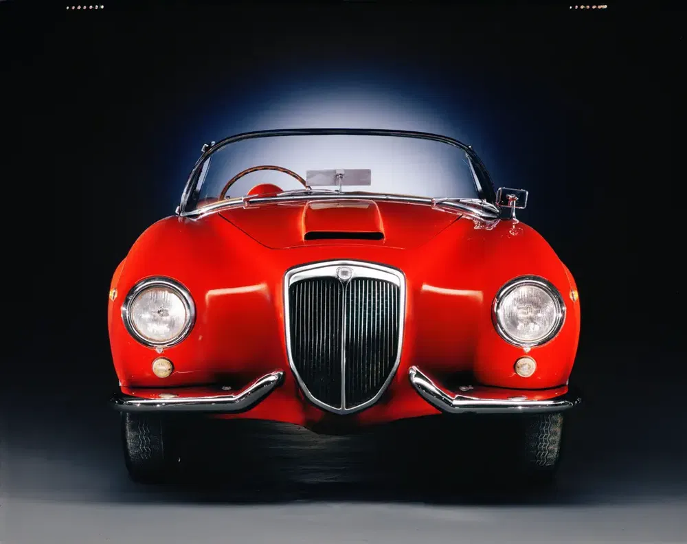 Lancia Aurelia rouge classique sur fond noir, vue de face élégante et intemporelle.